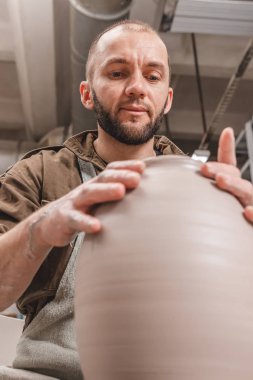 Potter, stüdyodaki çömlekçi çemberinde büyük bir sürahi beyaz kil yapıyor. Yaratıcılık ve sanat kavramı, dikey fotoğraf.