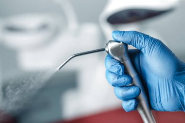 Elinde hava şırıngası tutan mavi eldivenli dişçinin kadın eli, kliniğin arka planında diş hekimliği ve fotokopi alanı olan bulanık diş sağlığı konsepti.