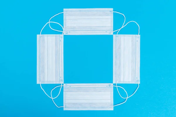 Frame made with many medical masks of blue color on background, concept of protection against flu, viruses and other diseases with copy space, top view