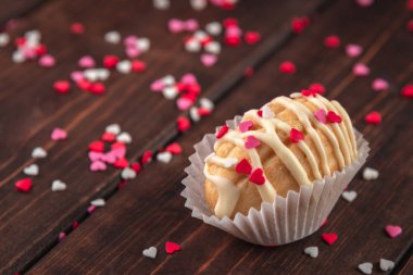 Ev yapımı fındık şekilli kremalı kurabiye, arka plan olarak ahşap masa üzerindeki çikolata kreması, kırmızı, gül ve beyaz şeker serpiştirme kalpleri, pasta ve fırın için kırsal tarzda süsleme