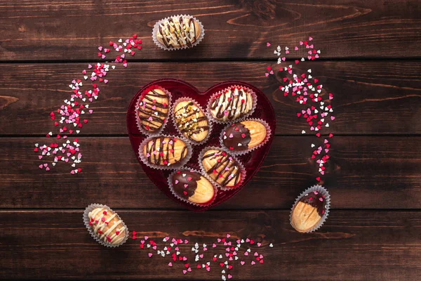 Ev yapımı kurabiyelerin yaptığı çerçeve kremalı fındık şekilli, ahşap masa üzerindeki çikolata kreması arka plan olarak, kırmızı, gül ve beyaz şeker serpiştirilmiş kalpler, pasta ve fırın için kırsal tarzda dekorasyon — Stok fotoğraf