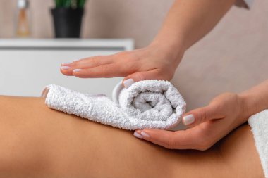 Kadın masör elleri genç bir kadının sırtına beyaz havlu koyuyor. Spa salonunda tedavinin tadını çıkarıyorlar. Sakinlik ve rahatlama atmosferi, masaj anlayışı, vücut bakımı ve güzellik.