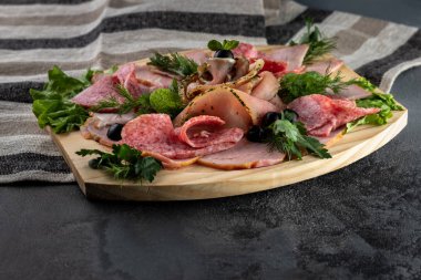 Salam, jambon, maydanozlu jambon ve zeytin gibi dilimlenmiş lezzetli et karışımı. Masa örtüsü ve gri çimento arka planında tahta bir kesme tahtası.