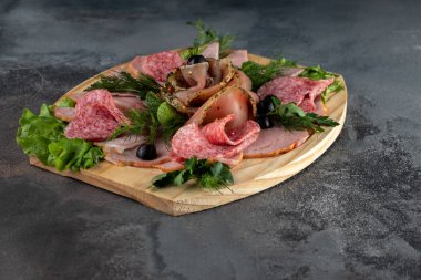 Yan manzara dilimlenmiş lezzetli et karışımı salam, pastırma ve maydanozlu jambon ve zeytin gibi gri çimento arka planında tahta kesme tahtasında fotokopi alanı ile.