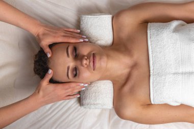 Gözleri kapalı, kalın kaşları ve kafa masajı sırasında mükemmel bir teni olan, beyaz havluyla arka planda dinlenen, güzellik fotoğrafı konsepti cilt bakımı ve spa tedavisi olan güzel bir kız.