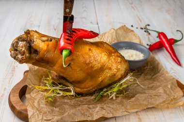 Ahşap kesim tahtasının üzerinde bıçak ve biber soslu kızarmış domuz budu, kırsal tarzda beyaz arka plan, geleneksel Belarus restoranında menü, yatay fotoğraf