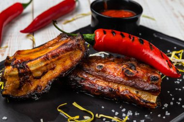 Kara tahtada kırmızı biber soslu yakın plan domuz pirzolası, kırsal alanda beyaz ahşap arka planda servis edilen ulusal yemek menüsü.