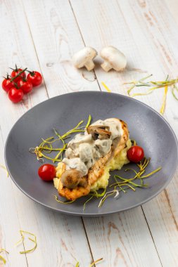 Kremalı mantar soslu ızgara tavuk göğsü. Narin patates püresi ve sulu vişneli domates. Kırsal tarzda beyaz ahşap arka planda ulusal yemek restoranının yemek menüsü.