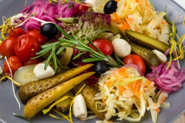 Ev yapımı turşulu aperatif, salatalık turşusu, sarımsak, soğan, zeytin, marul, domates, beyaz ahşap arka planda servis edilen, köy tarzı, ulusal gıda restoranında dilimlenmiş sebzeler.