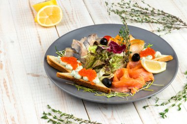 Beyaz ahşap arka planda yemek restoranının yemek menüsü, füme somon, balina ve ringa balıklı aperatif, krem peynirli buğday ekmeği, limon dilimli salata.