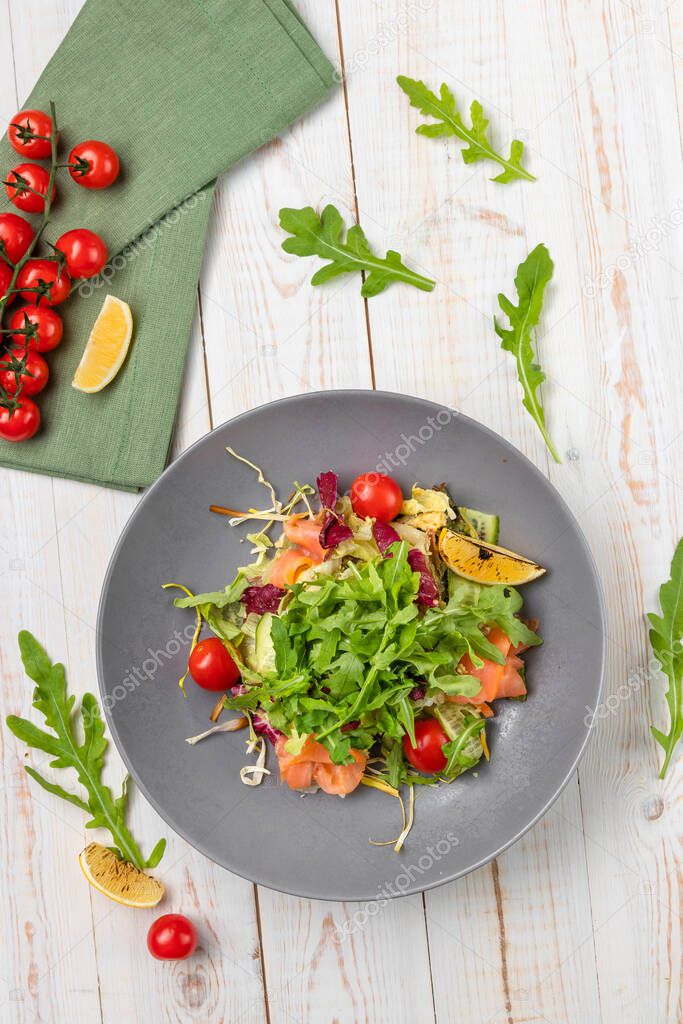 top view salmon mix salad with sesame-honey dressing, slices of fish, cherry tomatoes, arugula, pickled cucumber, lunch menu of national food restaurant on white wooden background in rustic style