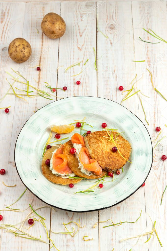 potato pancakes with salmon, cranberries and tartar sauce on white wooden background, lunch menu of food restaurant in rustic style