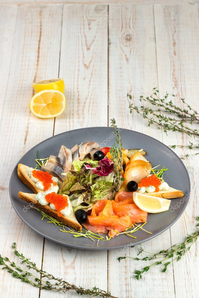 appetizer with smoked salmon, butterfish and herring, wheat croutons with cream cheese, mix salad with lemon slices, lunch menu of national food restaurant on white wooden background in rustic style