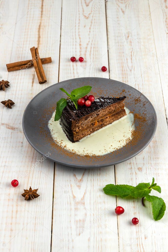 Slice of chocolate cake with cranberry on a plate. Background with delicious dessert of russian cuisine. Lunch menu of food restaurant on white wooden table in rustic style, side view