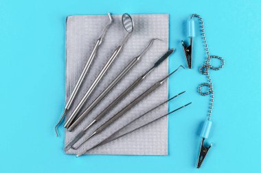 Metal dişçi aletleri, gri su geçirmez peçete ve mavi arka planda izole edilmiş ekipmanlar. Periodontal kaşifler, çelik, ağız aynası, cımbız ve diğer aletler. Diş bakımı konsepti