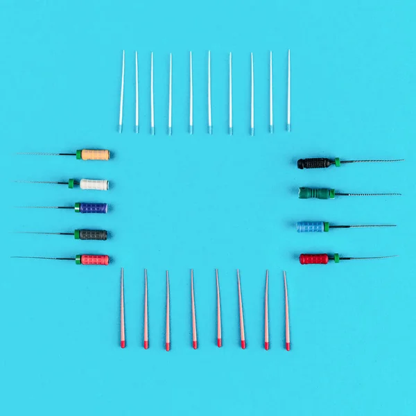 Set of dental needles for root canal treatment process on blue medical background, top view. Human teeth care and health concept