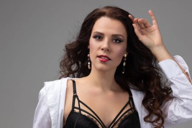 Çekici kız pozu, yakın plan gri arkaplandaki stüdyodur. Rüzgarda sallanan uzun kıvırcık saçlı esmer model. Kuaförde kuaförlük ve yüz bakımı kavramı