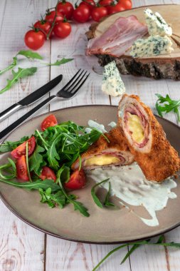 Domuz pastırmalı, peynirli, domatesli, roka soslu domuz eti ve bir restorandaki ahşap beyaz masada.