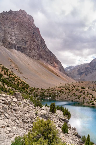 The beautiful mountain trekking road with clear blue sky and rocky hills and the view of Alaudin lake in Fann mountains in Tajikistan