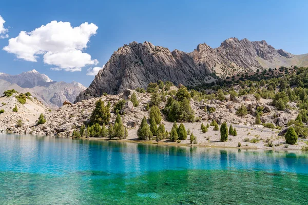 The beautiful mountain trekking road with clear blue sky and rocky hills and the view of Alaudin lake in Fann mountains in Tajikistan