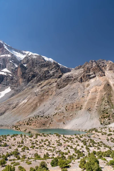 The beautiful mountain trekking road with clear blue sky and rocky hills and fresh mountain lake in Fann mountains in Tajikistan