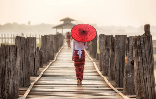 Mujer birmana sosteniendo paraguas rojo tradicional y caminando en U Bein Bridge — Foto de Stock