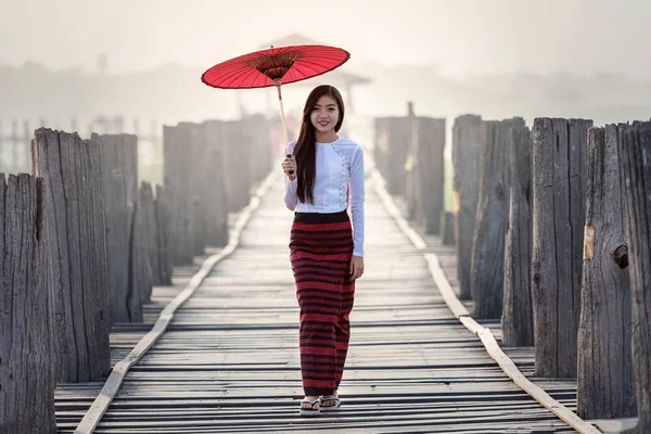 Burmese woman holding traditional red umbrella and walking on U Bein Bridge — Stock Photo, Image