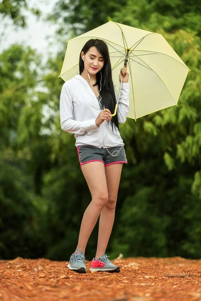 Азиатка слушает музыку с зонтиком — стоковое фото