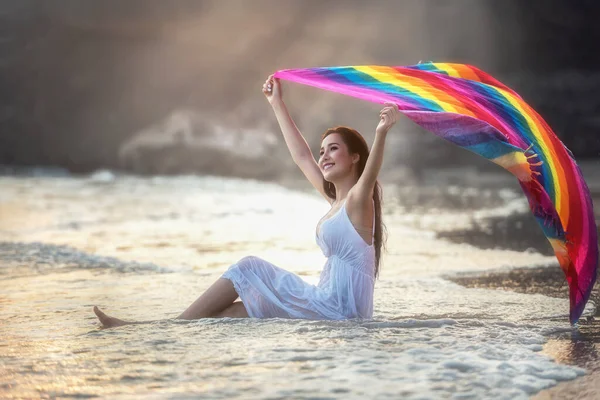 熱帯のビーチでリラックスした明るい虹色のサロンと白いドレスを着て若い女性の肖像画 休暇の日のコンセプト — ストック写真