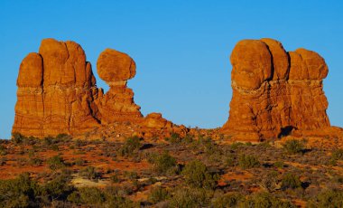 Arches Ulusal Parkı 'nda alışılmadık şekilli kumtaşı sütunu gökyüzüne doğru uzanıyor. Kayaların arasında yürüyen insanlar kolonların büyüklüğü hakkında fikir verir..