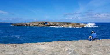 Bir adam kayalık bir sahilden derin sularda balık tutmak için olta ve olta kullanıyor..