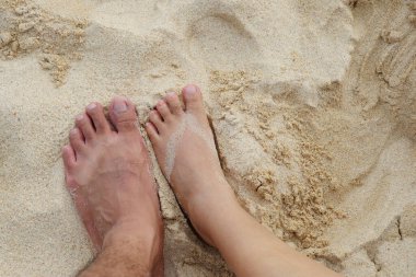 Kumsalda kumlara basan kadın ve erkeklerin ayakları..