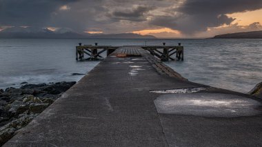 The old jetty at Portencross in Scotland and winter hills on the isle of Arran just as the sun goes down producing a dramatic sunset sky over the Clyde. clipart