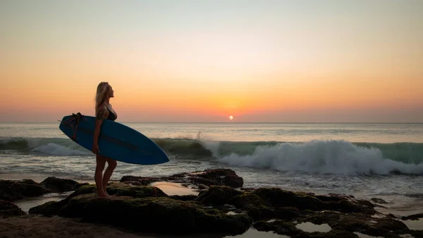Silhouette eines Surfermädchens mit Surfbrett am Strand. Sonnenuntergang. tegal wangi beach, bali, indonesien — Stockfoto