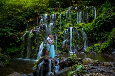 Tropikal ormanda şelalenin yanında kucaklaşan mutlu, çok kültürlü çift. Yavaş deklanşör hızı, hareket fotoğrafçılığı.