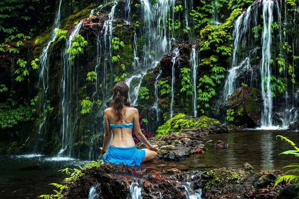 Jeune femme assise sur le rocher, pratiquant le yoga près de la cascade. Mains dans le mudra gyan. Cascade de Banyu Wana Amertha, Bali. Vue de dos . — Photo