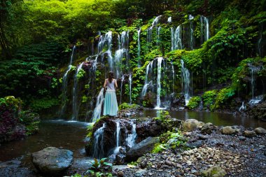 Tropikal ormandaki şelalede genç bir gezgin kadın. Arkadan bak. Banyu Wana Amertha Şelalesi Wanagiri, Bali. Yavaş deklanşör hızı, hareket fotoğrafçılığı.