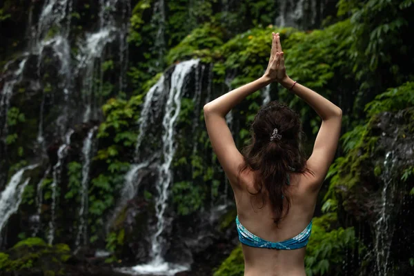 Primo piano della donna yoga alzare le braccia con mudra namaste di fronte alla cascata. Vista da dietro. Cascata di Banyu Wana Amertha Wanagiri, Bali, Indonesia . — Foto Stock