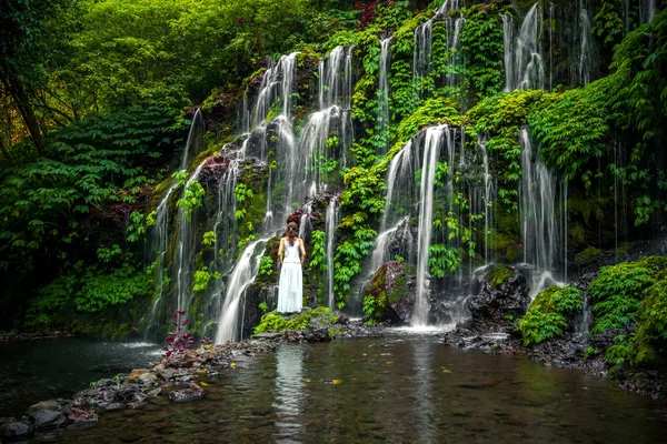 Tropikal ormandaki şelalede genç bir gezgin kadın. Arkadan bak. Banyu Wana Amertha Şelalesi Wanagiri, Bali. Yavaş deklanşör hızı, hareket fotoğrafçılığı.