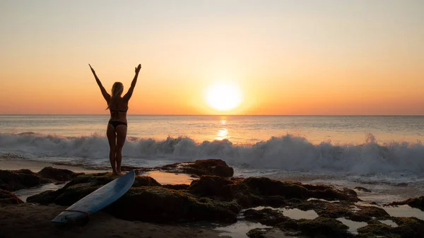 Silhouette einer Frau. aufgeregte junge Frau, die am Strand vor dem Ozean die Arme hebt. Blick von hinten. Sonnenuntergang am Strand. bali, indonesien. — Stockfoto