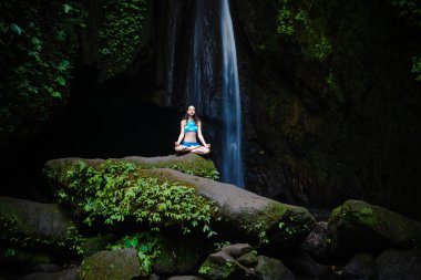 Genç beyaz kadın meditasyon yapıyor, şelalede yoga yapıyor. Gyan Mudra. Leke Leke Şelalesi, Bali, Endonezya. 