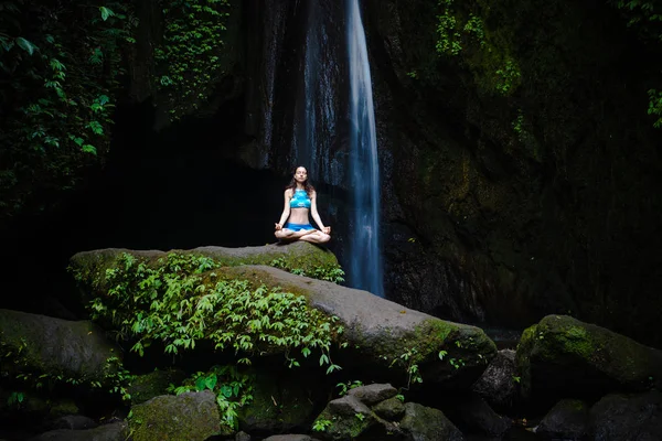 Young Caucasian woman meditating, practicing yoga at waterfall. Gyan mudra. Leke Leke waterfall, Bali, Indonesia. — Stock Photo, Image