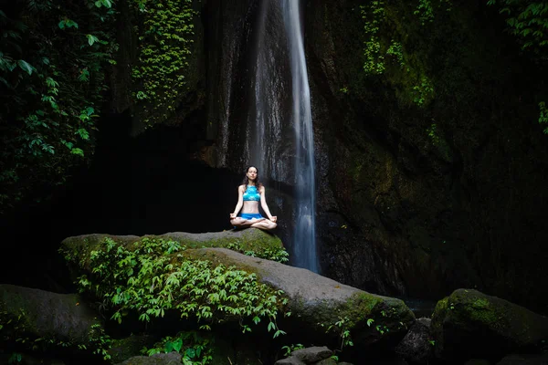 Genç beyaz kadın meditasyon yapıyor, şelalede yoga yapıyor. Gyan Mudra. Leke Leke Şelalesi, Bali, Endonezya. 