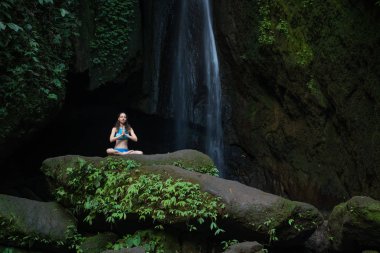 Genç beyaz kadın meditasyon yapıyor, şelalede yoga yapıyor. Eller namaste mudra 'da. Leke Leke Şelalesi, Bali, Endonezya. 