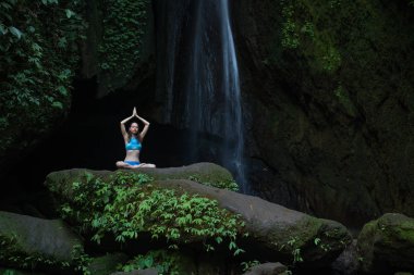 Genç beyaz kadın meditasyon yapıyor, şelalede yoga yapıyor. Namaste Mudra 'da eller havaya. Leke Leke Şelalesi, Bali, Endonezya. 