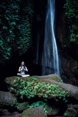 Genç beyaz kadın meditasyon yapıyor, şelalede yoga yapıyor. Eller namaste mudra 'da. Leke Leke Şelalesi, Bali, Endonezya. 