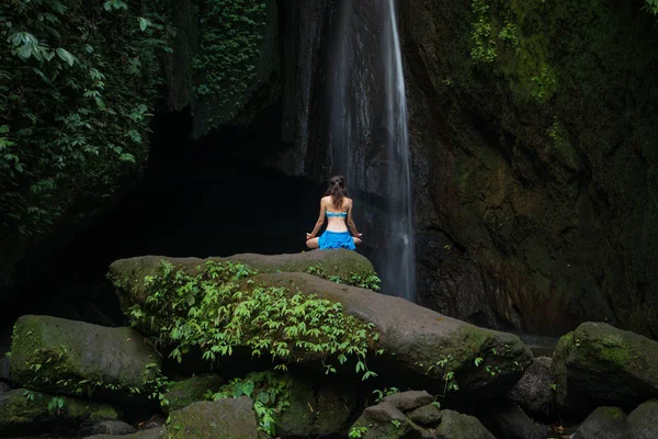 Jeune femme assise sur le rocher, pratiquant le yoga près de la cascade. Mains dans le mudra gyan. Chute d'eau Leke Leke, Bali. Vue de dos . — Photo