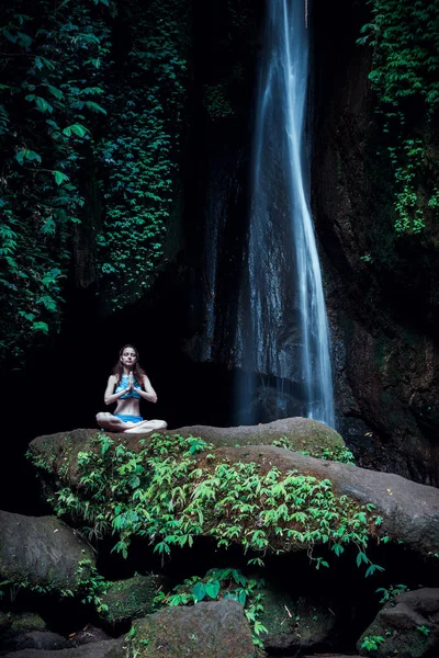 Genç beyaz kadın meditasyon yapıyor, şelalede yoga yapıyor. Eller namaste mudra 'da. Leke Leke Şelalesi, Bali, Endonezya. 