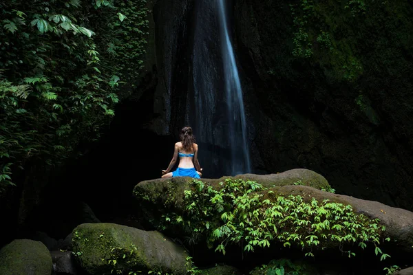 Jeune femme assise sur le rocher, pratiquant le yoga près de la cascade. Mains dans le mudra gyan. Chute d'eau Leke Leke, Bali. Vue de dos . — Photo
