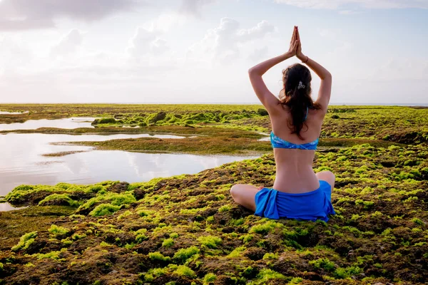 Giovane donna, meditare, praticare yoga e pranayama in spiaggia. Pratica di yoga all'alba. Mani in alto nel mudra namaste. Vista da dietro. Spiaggia di Melasti, Bali — Foto Stock